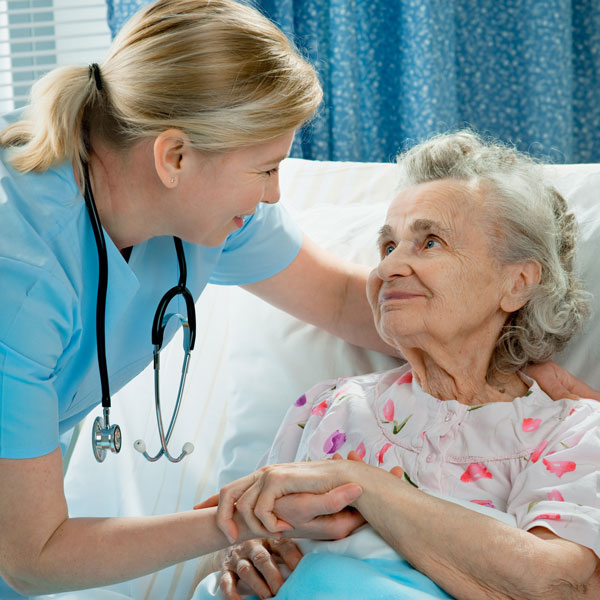 Female nurse caring for an elderly woman in a hospital bed.